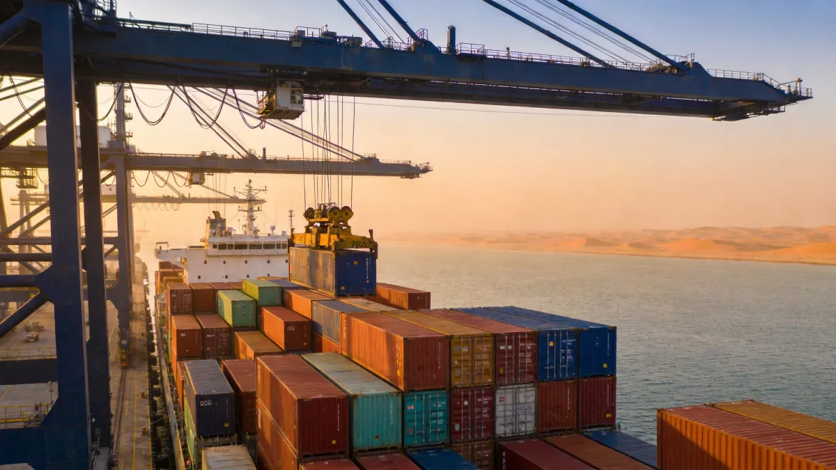 Gantry cranes loading colorful shipping containers onto a cargo vessel at a Gulf port at sunset
